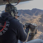 Participants aims a fully automatic machine gun from the open door of a helicopter over the Mojave Desert during Gunship Helicopters’ tactical aerial shooting tour in 2025.