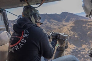 Participants aims a fully automatic machine gun from the open door of a helicopter over the Mojave Desert during Gunship Helicopters’ tactical aerial shooting tour in 2025.