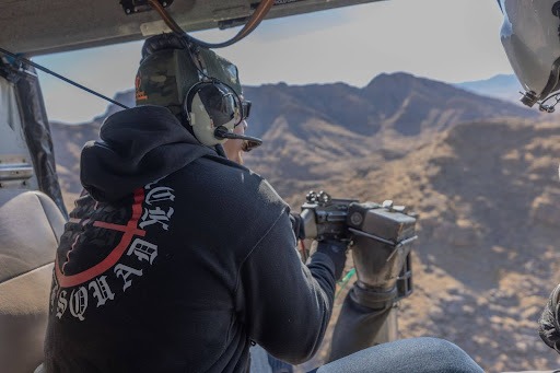Participants aims a fully automatic machine gun from the open door of a helicopter over the Mojave Desert during Gunship Helicopters’ tactical aerial shooting tour in 2025.