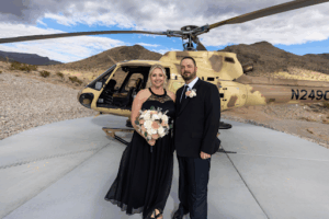 Bride and groom pose in front of a tactical helicopter at Gunship Helicopters’ desert landing zone after their unique Las Vegas helicopter wedding experience.