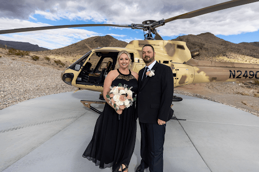 Bride and groom pose in front of a tactical helicopter at Gunship Helicopters’ desert landing zone after their unique Las Vegas helicopter wedding experience.