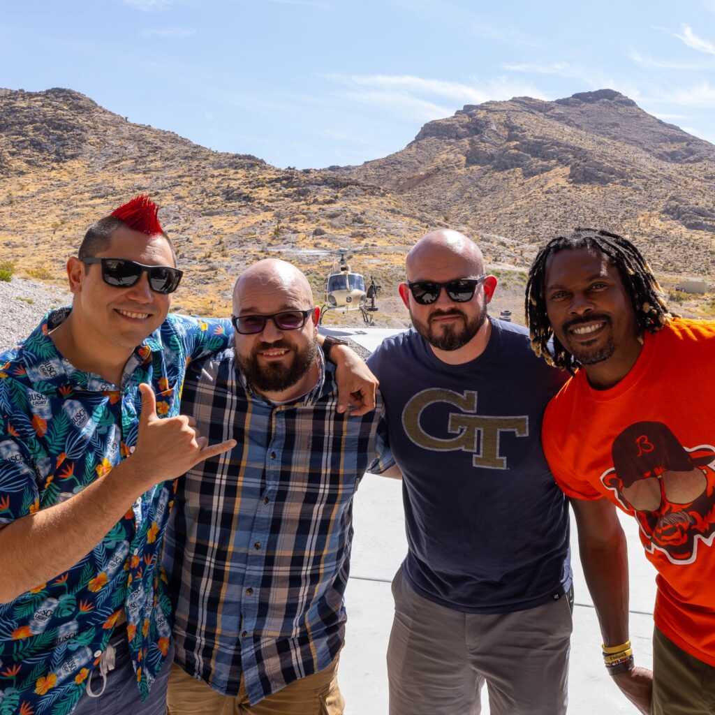 deluxe squad up - Four friends pose in front of helicopter at Gunship Helicopters outdoor shooting range in Las Vegas