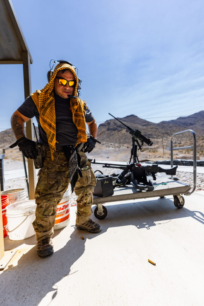 Veteran range safety officer supporting veteran affairs at Gunship Helicopters’ outdoor shooting range in Las Vegas, standing beside mounted heavy machine guns in the Mojave Desert.