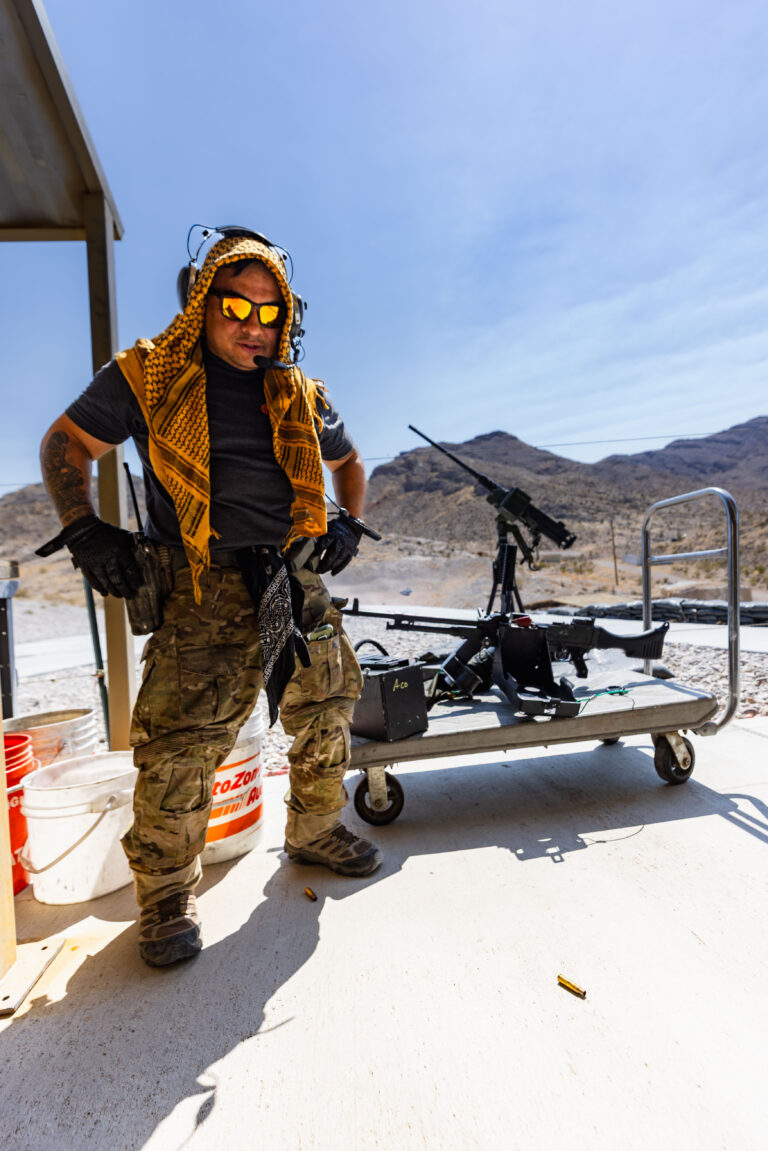 Veteran range safety officer supporting veteran affairs at Gunship Helicopters’ outdoor shooting range in Las Vegas, standing beside mounted heavy machine guns in the Mojave Desert.