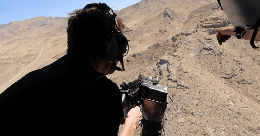 Guest firing fully automatic weapon from open-door helicopter over Mojave Desert during aerial shooting adventure in Las Vegas